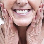 close up of an older woman holding her cheeks and smiling with dentures