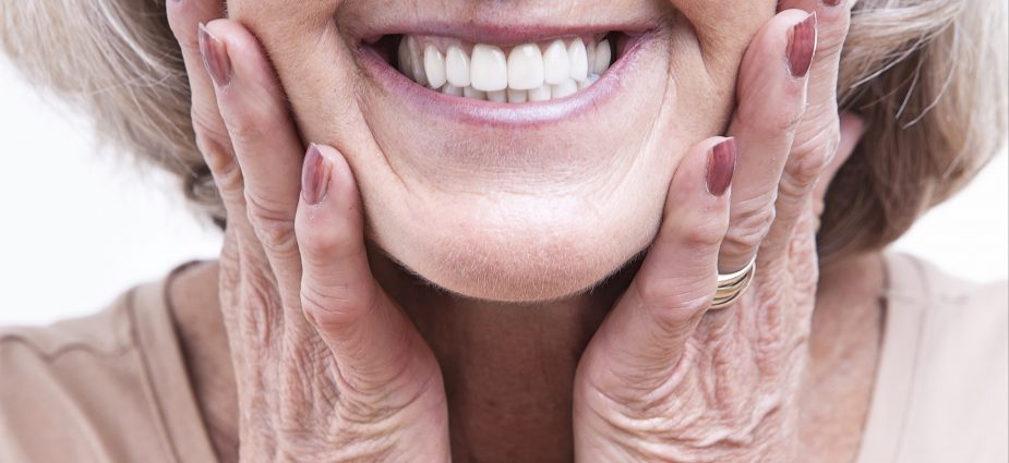 close up of an older woman holding her cheeks and smiling with dentures