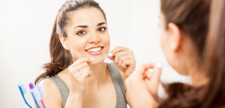 woman applying whitening strip in bathroom mirror