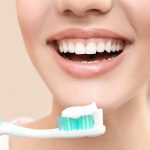 woman smiling holding toothbrush with toothpaste on it